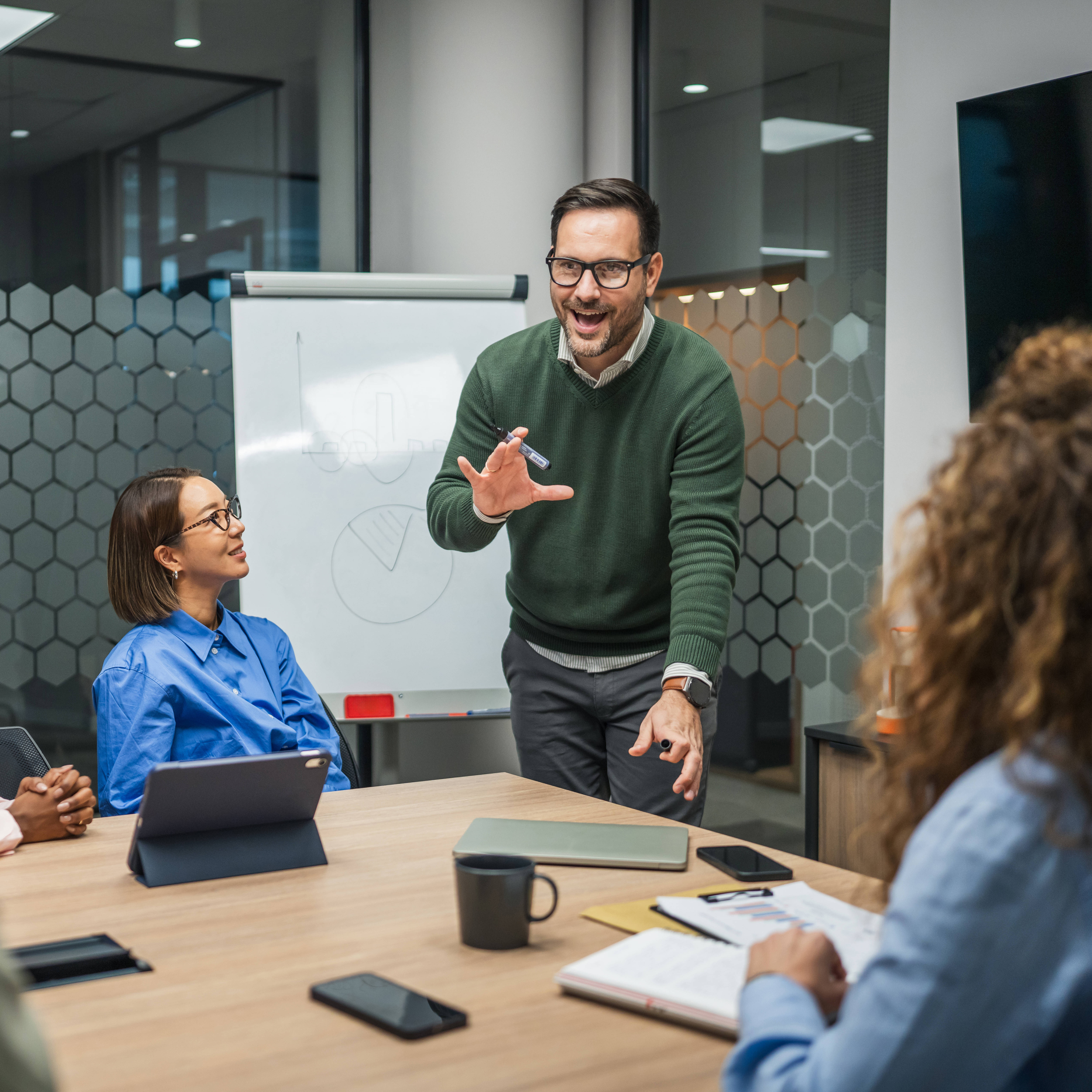 Business presenter standing, discussing ideas and gesturing during a corporate meeting, engaging with diverse colleagues listening and collaborating around a conference table in a modern office